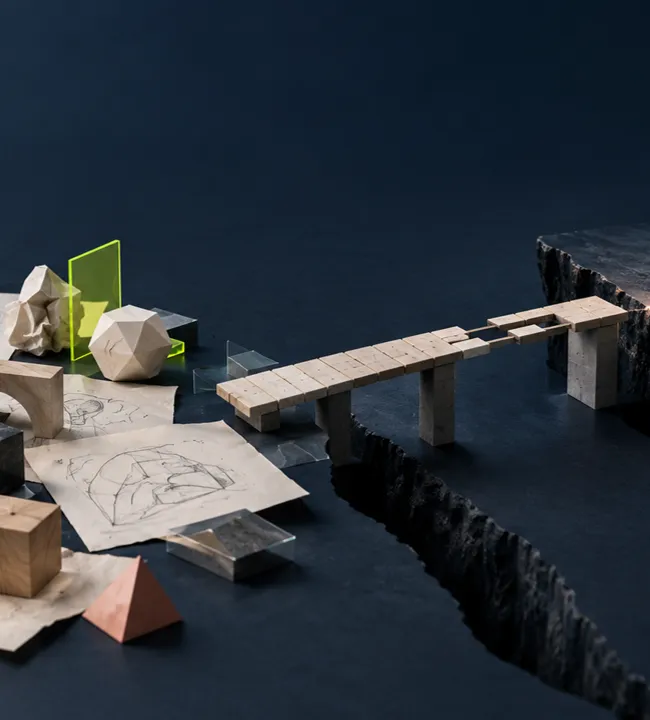Maqueta de un puente que une dos lados de una grieta, rodeado de bocetos y piezas
